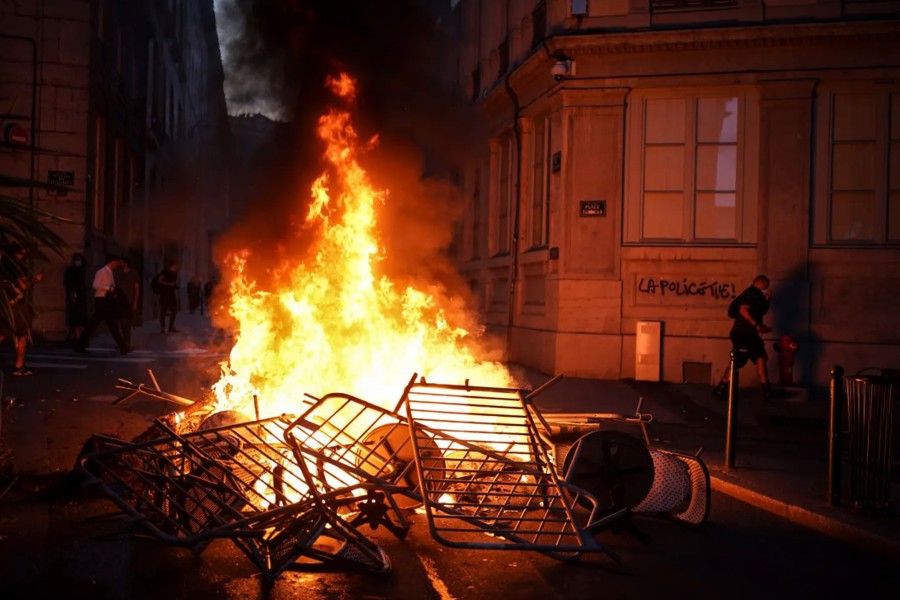Hàng rào bị người biểu tình đốt cháy, bên cạnh một bức tường có dòng chữ "cảnh sát giết", ở trung tâm thành phố Lyon, miền Trung nước Pháp, hôm 1/7. Ảnh: AP