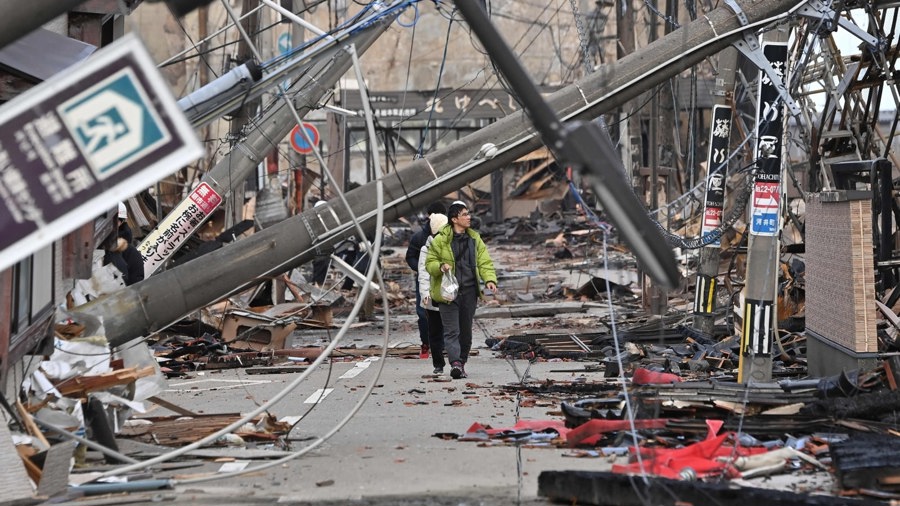 Người dân băng qua các cột điện bị đổ và các tòa nhà hư hỏng ở thành phố Wajima, tỉnh Ishikawa vào ngày 4/1/2024, sau khi trận động đất lớn 7,5 độ richter xảy ra ở vùng Noto thuộc tỉnh này vào ngày đầu năm mới. Ảnh: AFP