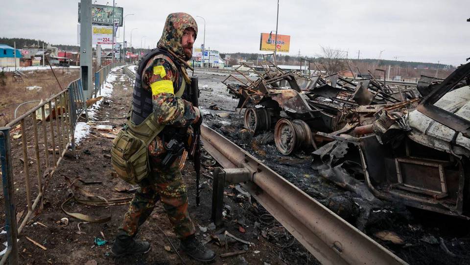 Một người đ&agrave;n &ocirc;ng c&oacute; vũ trang đứng b&ecirc;n phần c&ograve;n lại của một chiếc xe qu&acirc;n sự Nga ở Bucha, gần thủ đ&ocirc; Kiev, Ukraine, ng&agrave;y 1/3. Ảnh: AP
