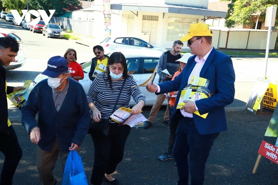 Ứng cử viên John Koukoulis (bìa phải) đứng bên ngoài địa điểm bỏ phiếu để thuyết phục cử tri.