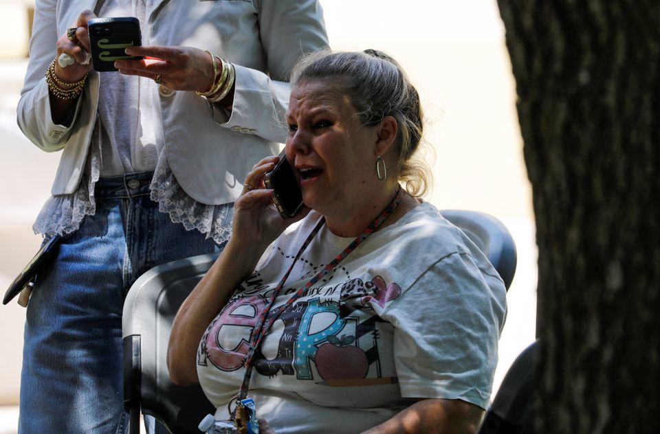 Một người phụ nữ n&oacute;i chuyện điện thoại b&ecirc;n ngo&agrave;i hiện trường trường học. Ảnh: Reuters