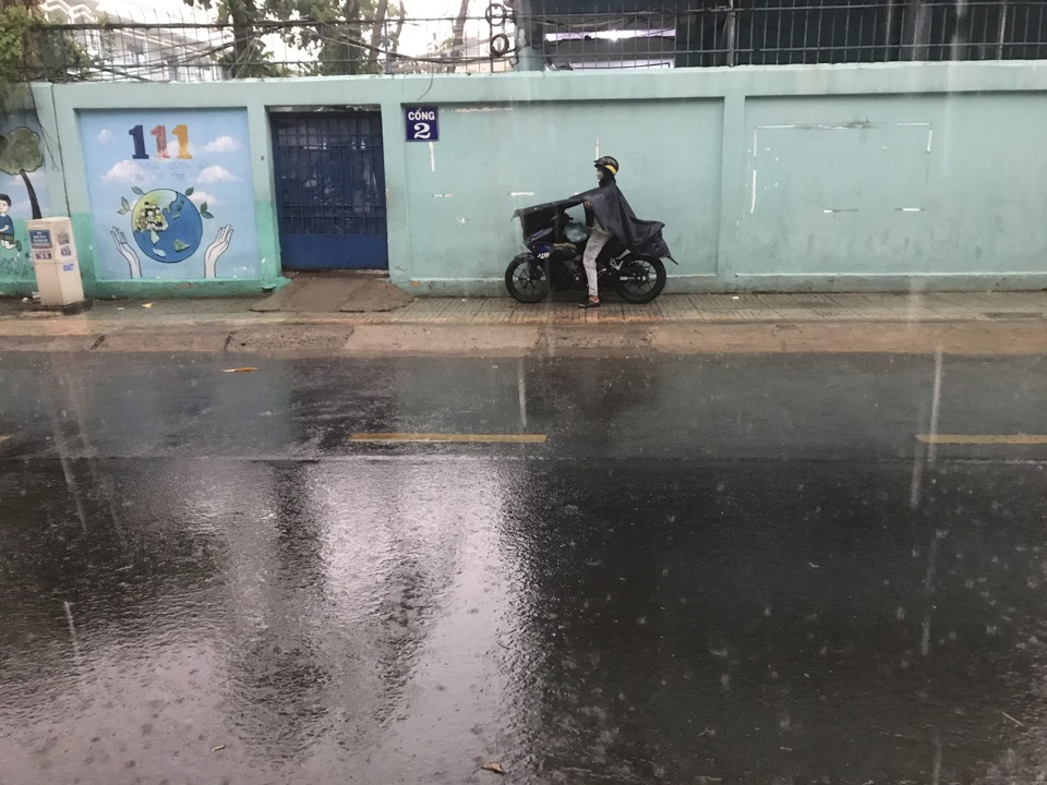 Một phụ huynh mặc &aacute;o mưa chờ đ&oacute;n con v&agrave;o chiều 8/5, trước cổng Trường THCS B&igrave;nh T&acirc;y (quận 6, TP Hồ Ch&iacute; Minh). Ảnh: T&acirc;n Tiến.