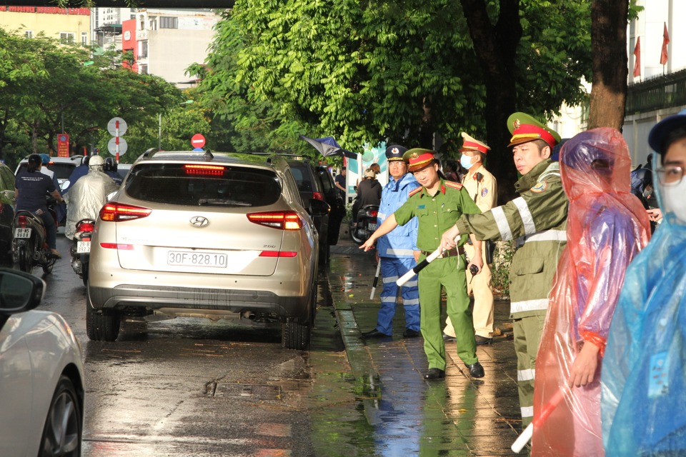 Lực lượng chức năng phường Dịch Vọng, quận Cầu Giấy đội mưa tổ chức hướng dẫn giao th&ocirc;ng tại điểm thi Trường THCS Dịch Vọng. Ảnh: C&ocirc;ng Tr&igrave;nh