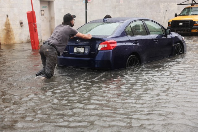 Người đ&agrave;n &ocirc;ng đẩy chiếc xe qua con đường ngập tại khu phố Red Hook, Brooklyn, New York. Ảnh: AFP &nbsp;