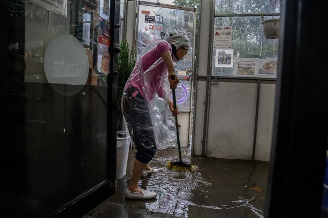 Một phụ nữ đẩy nước ra khỏi cửa h&agrave;ng ở khu Brooklyn. Ảnh: AFP &nbsp;
