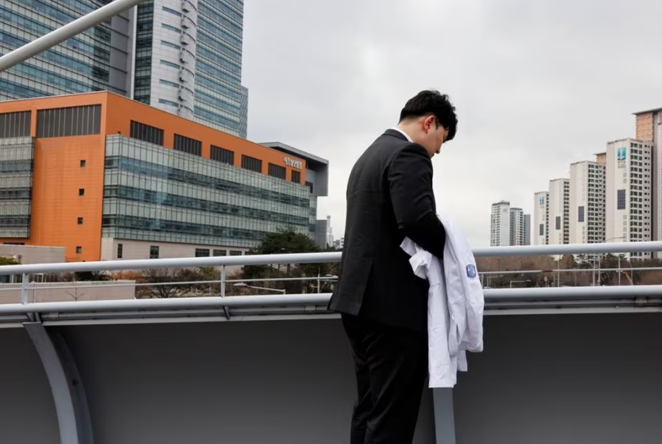 Ryu O. Hada, 25 tuổi, cầm chiếc &aacute;o kho&aacute;c trắng đứng b&ecirc;n ngo&agrave;i bệnh viện nơi anh l&agrave;m việc ở Seoul. Ảnh: Reuters