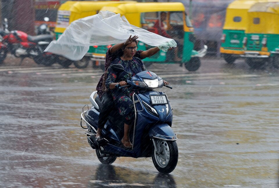 Người đi l&agrave;m sử dụng tấm nilon để che mưa khi đi qua con đường ngập nước ở Ahmedabad, Ấn Độ. Ảnh: Reuters.