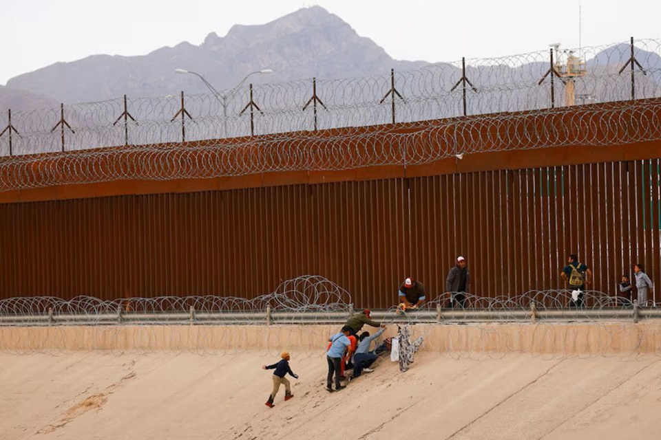 Người di cư tìm cách vượt qua hàng rào biên giới giữa Mỹ và Mexico. Ảnh: Reuters