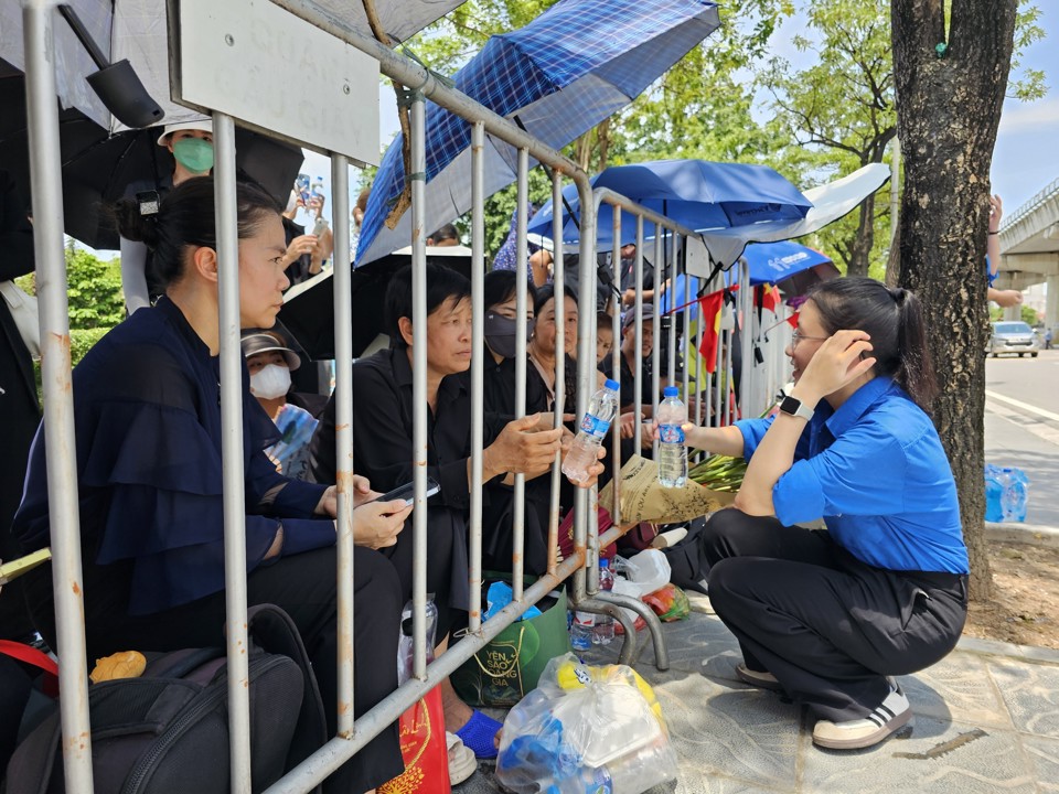 Người d&acirc;n b&ecirc;n ngo&agrave;i Nghĩa trang Mai Dịch nhận nước uống miễn ph&iacute; từ thanh ni&ecirc;n t&igrave;nh nguyện. Ảnh: Qu&acirc;n Thủy