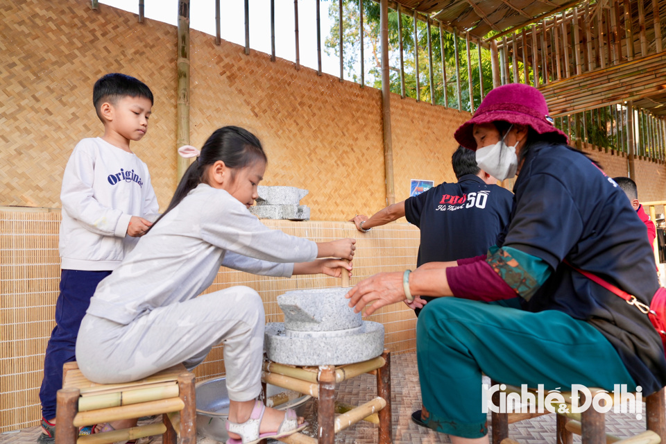 Nhiều gian h&agrave;ng l&agrave;ng nghề c&oacute; những trải nghiệm cho người d&acirc;n v&agrave; du kh&aacute;ch. Một em nhỏ tham gia trải nghiệm xay bột bằng cối đ&aacute;.